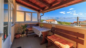 A balcony with wooden benches, a table with a polka dot tablecloth, potted plants, and a view of mountains. - Apartments Ruzica F (Lopar)