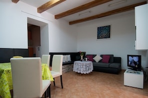 Una sala de estar con sofá, una mesa de comedor con sillas, televisor y una mesita con un florero.