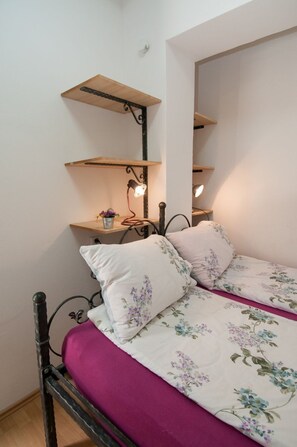Une chambre à coucher avec un lit, une table de chevet et une étagère avec une lampe.