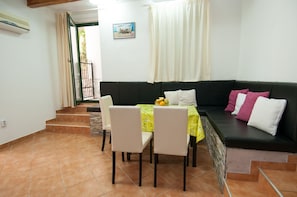 Un comedor con una mesa dispuesta para dos personas, un sofá negro con cojines, y una escalera que lleva a un espacio al aire libre.