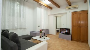 Een woonkamer met een bank, een salontafel met wijnflessen en glazen, een televisie op een dressoir en een houten garderobe.
