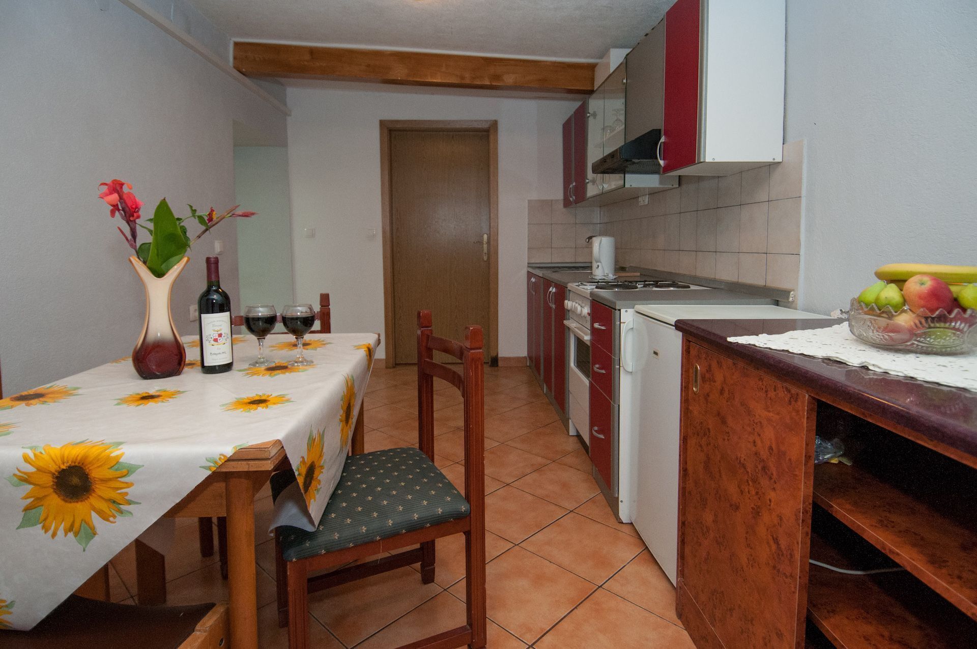A compact kitchen with a dining area, featuring a table set with wine glasses and a vase with flowers.