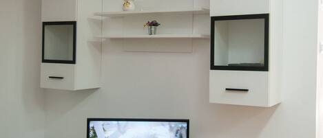 A modern living room with a flat-screen TV, white cabinetry, and a tiled floor.