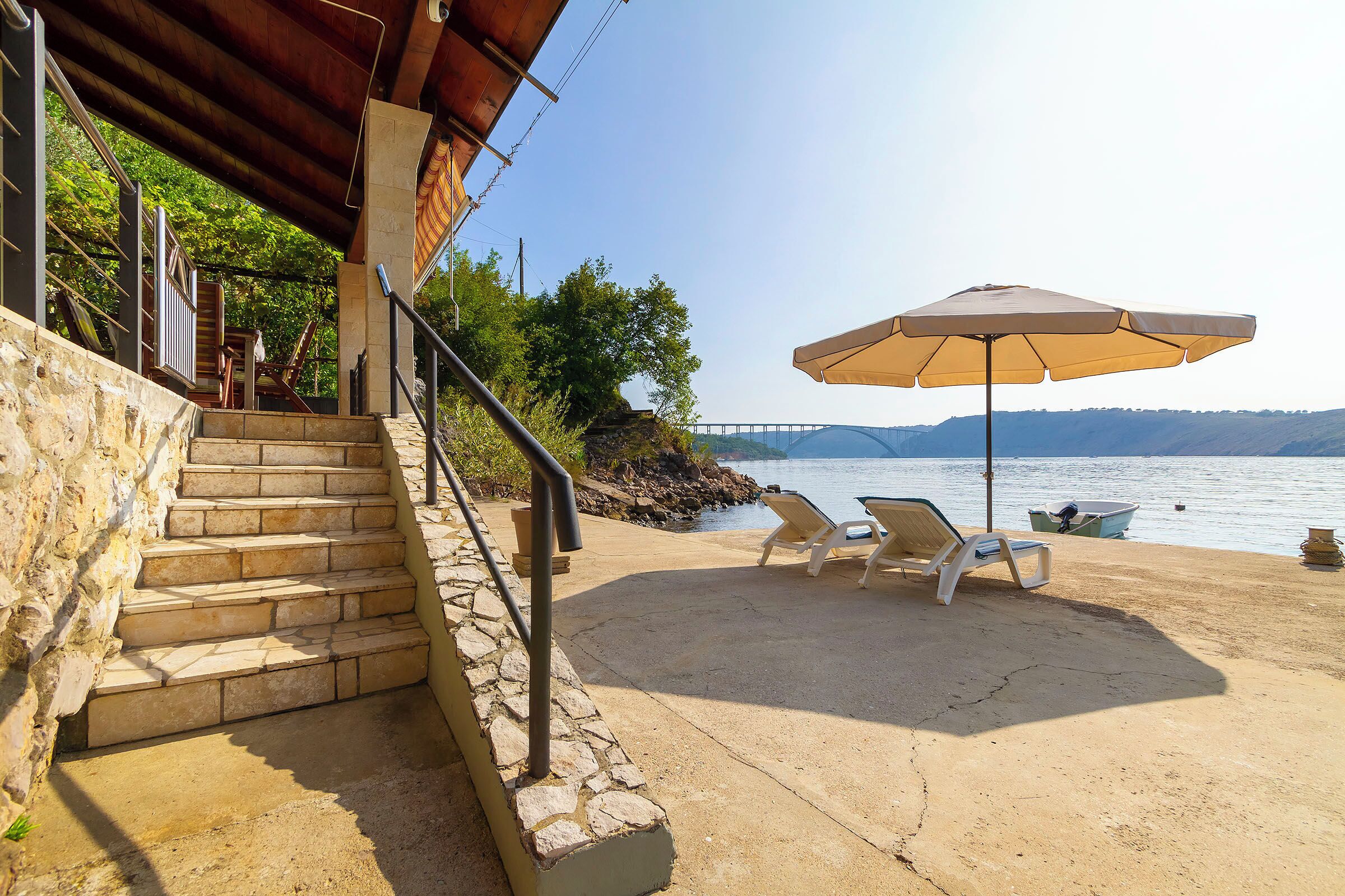 A concrete staircase leading to a beach area with lounge chairs and a large umbrella.