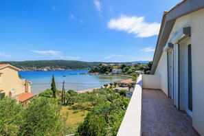 A balcony with a view of a coastal area, including a body of water and distant buildings. - Apartments Mirjana T (Rab)