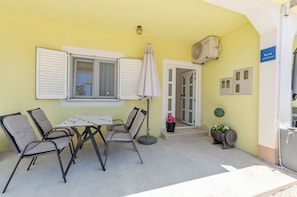 Een geel gevelpand met een tafel, stoelen, een parasol en een bloempot.