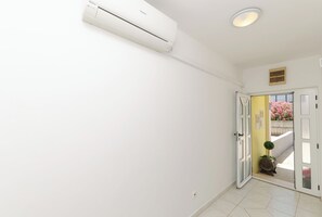 En hall med en vit luftkonditioneringsenhet, en dörr som leder ut och en liten krukväxt.