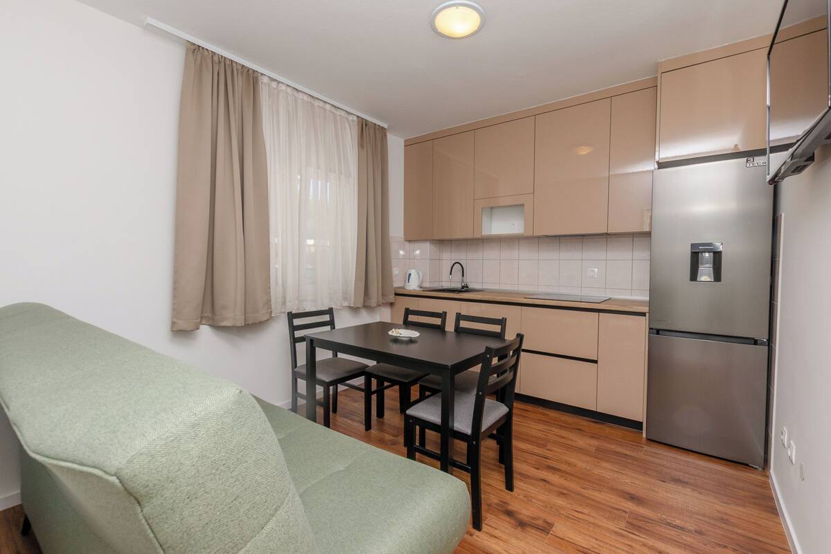 A compact kitchen with a dining table, chairs, a sofa, and a refrigerator.