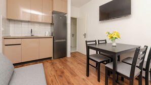 Une cuisine moderne avec des meubles de couleur beige, un réfrigérateur en acier inoxydable et un coin repas comprenant une table et des chaises.