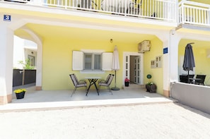 A yellow building with a balcony, a table with chairs, and a door. - Apartments Lemon (Vodice)