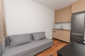 A compact kitchen with a grey sofa, wooden flooring, and a stainless steel refrigerator. - Apartments Lemon (Vodice)