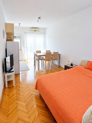 A hotel room with a bed, a television, a dining table with chairs, and a kitchen area. - Apartment Prcela 1 (Primosten)