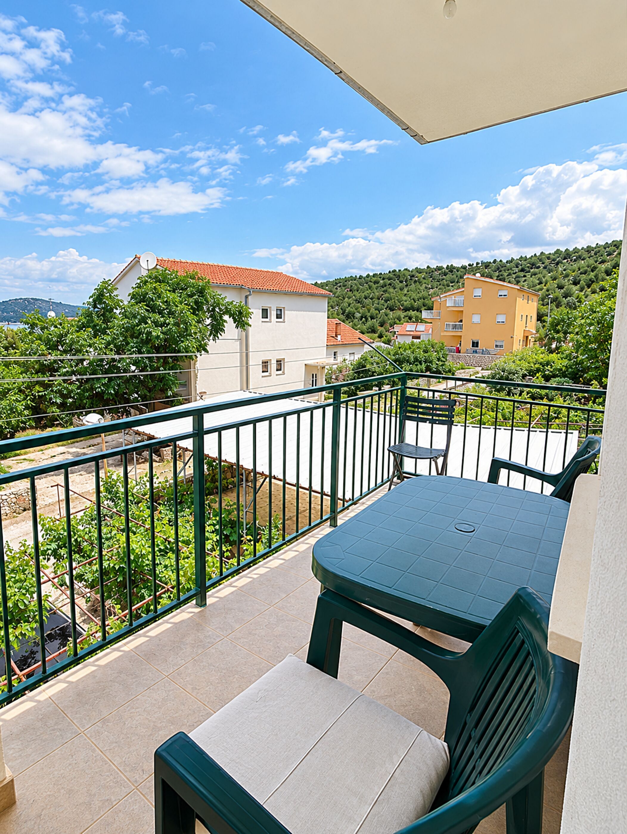A balcony with a table and chairs, a view of buildings, and a clear sky.