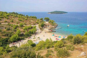 Une plage côtière avec un sentier menant au rivage, des bateaux et une petite île au loin.