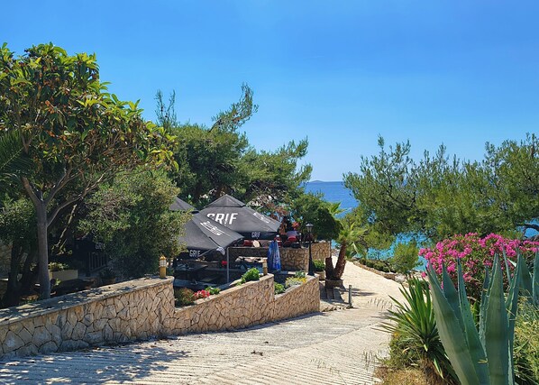 Un espace extérieur aménagé avec des sièges, situé en bord de mer, doté de murs en pierre et de parasols portant l’inscription « GRIF ».
