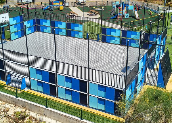 A multi-story building with a sports court, surrounded by a fence and greenery. - Apartment Prcela 1 (Primosten)