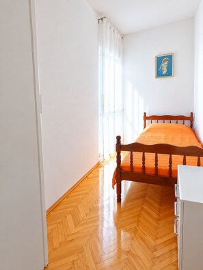 Een slaapkamer met een houten bed, witte muren, een houten vloer en een raam met gordijnen.