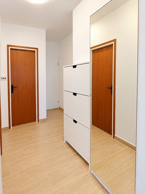 Een gang met houten deuren, een witte garderobe en een spiegel die de deur weerspiegelt.