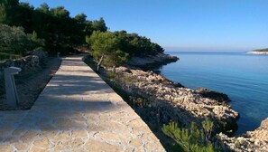 Un sentier de pierres mène à une côte rocheuse bordée d’une eau d’un bleu limpide.