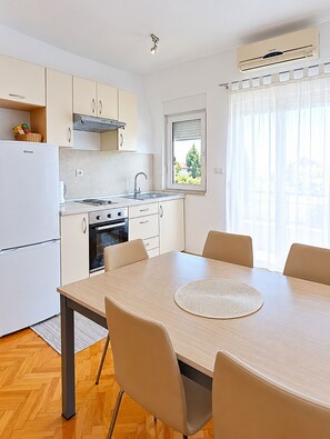 Une cuisine moderne avec des meubles blancs, un four encastré et un coin repas comprenant une table ronde et des chaises.