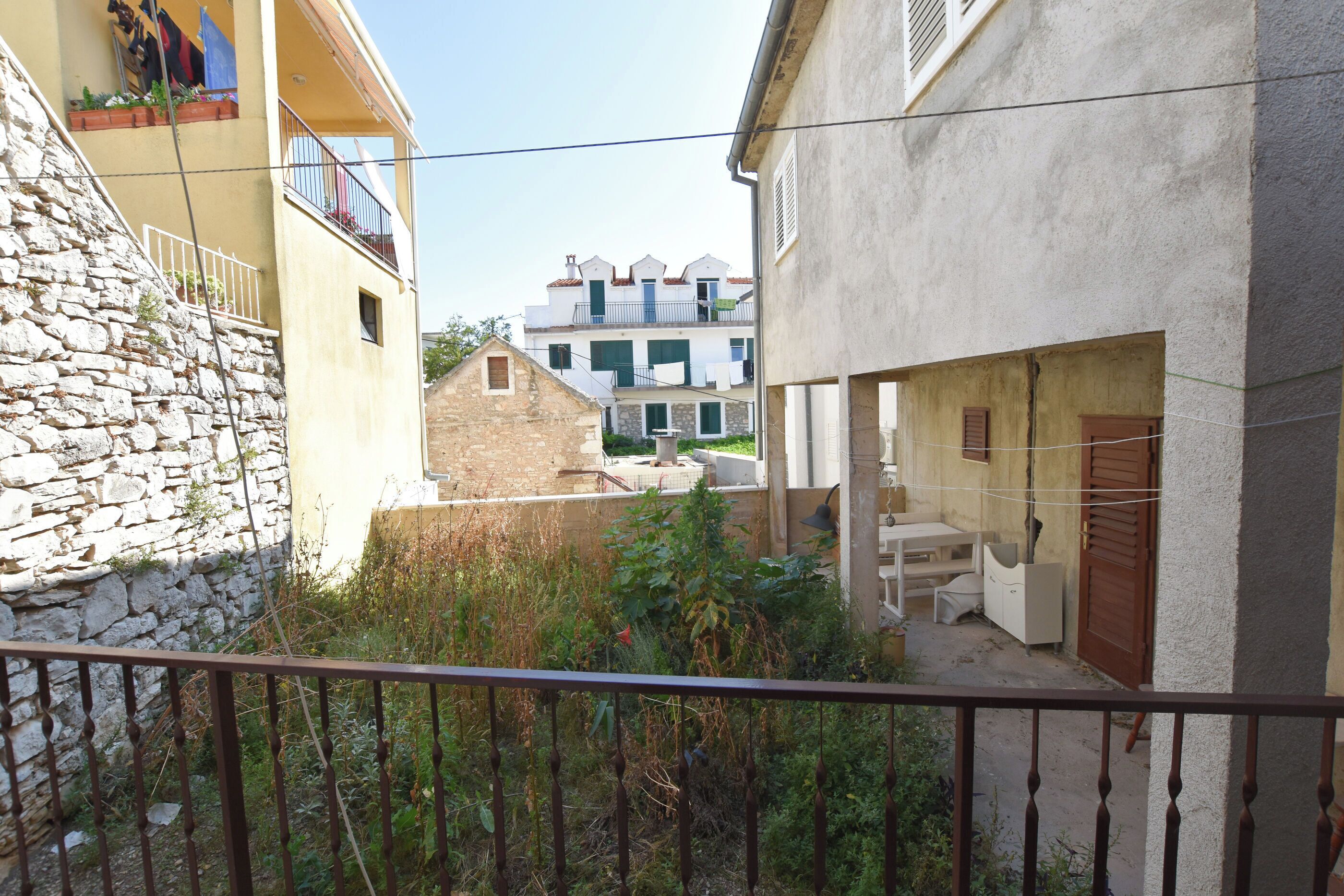 Una calle estrecha con edificios de piedra, un balcón con barandilla y un pequeño jardín.