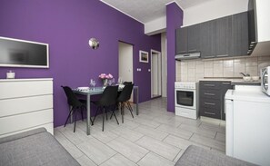 A modern kitchen with purple walls, a dining area with a table and chairs, and a white refrigerator. - Apartment Love (Dugi Rat)