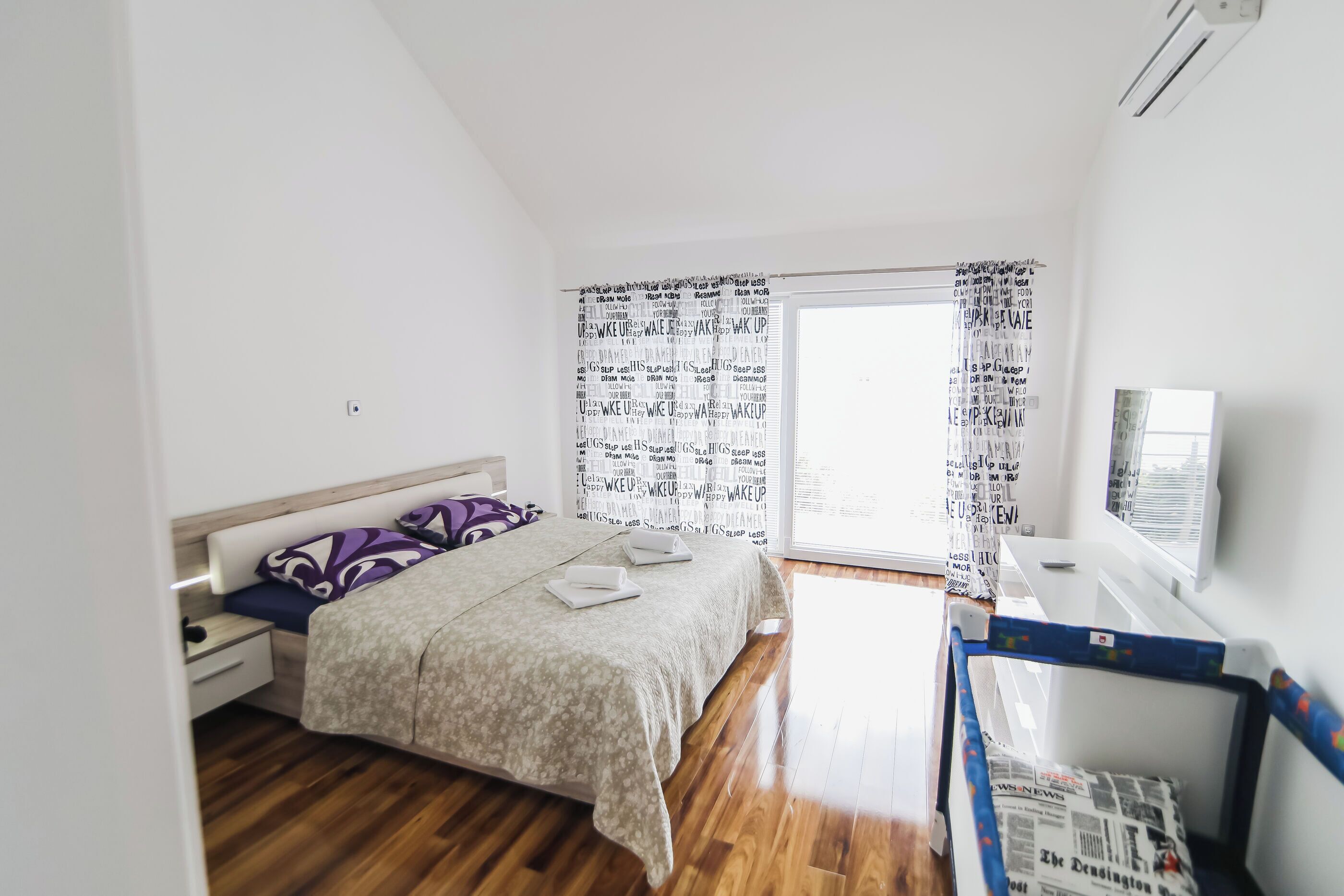 Una camera da letto con un letto, un comodino, una cassettiera, una finestra con tende e una TV a parete.