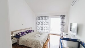 Una camera da letto con un letto, un comodino, una cassettiera, una finestra con tende e una TV a parete.