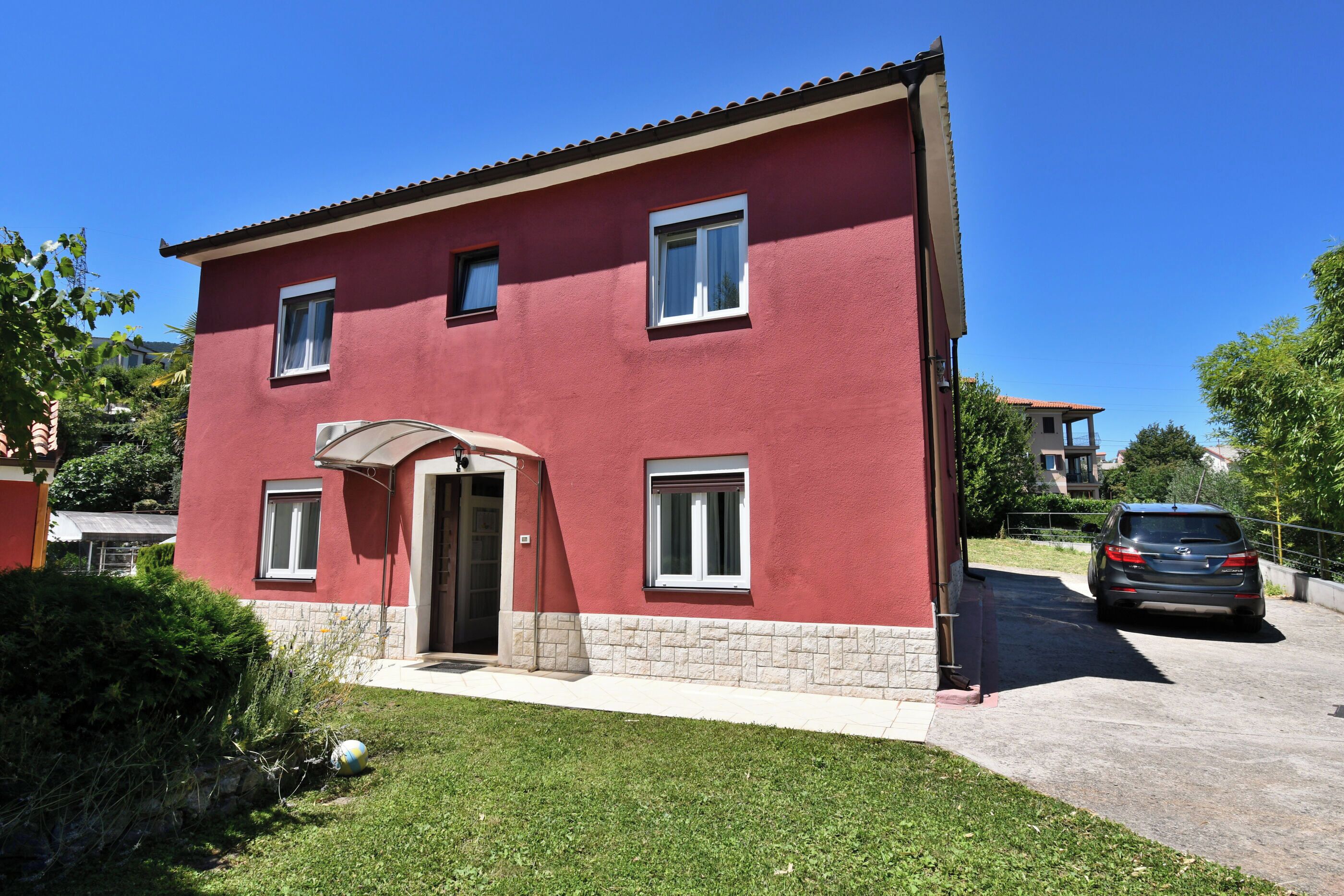 A red two-story building with a front door, windows, and a car parked in the driveway.