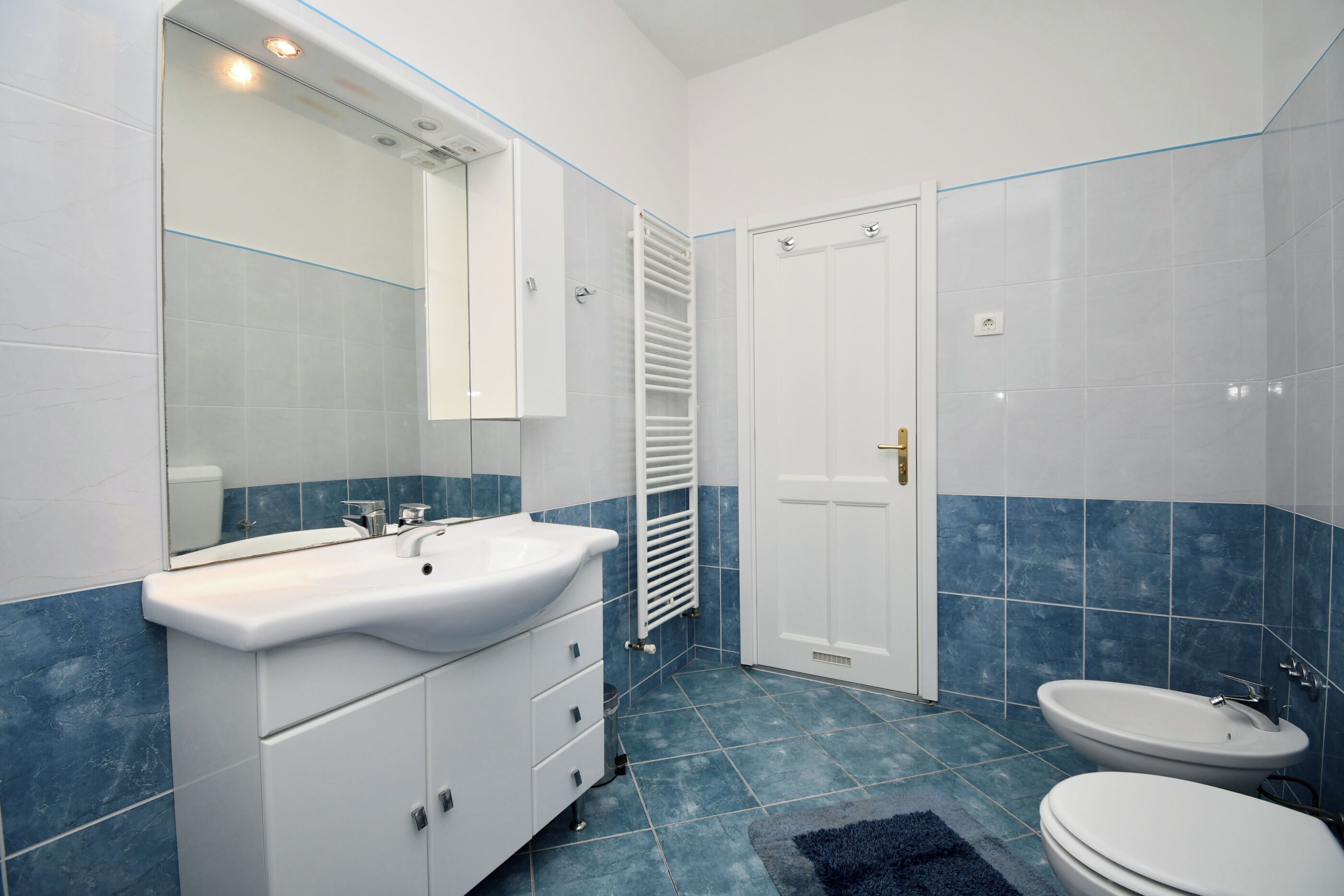 A bathroom with a white sink, a mirror, a white toilet, and a blue-tiled floor.