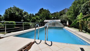 Una piscina con escaleras metálicas, rodeada de vegetación y un cielo azul despejado.