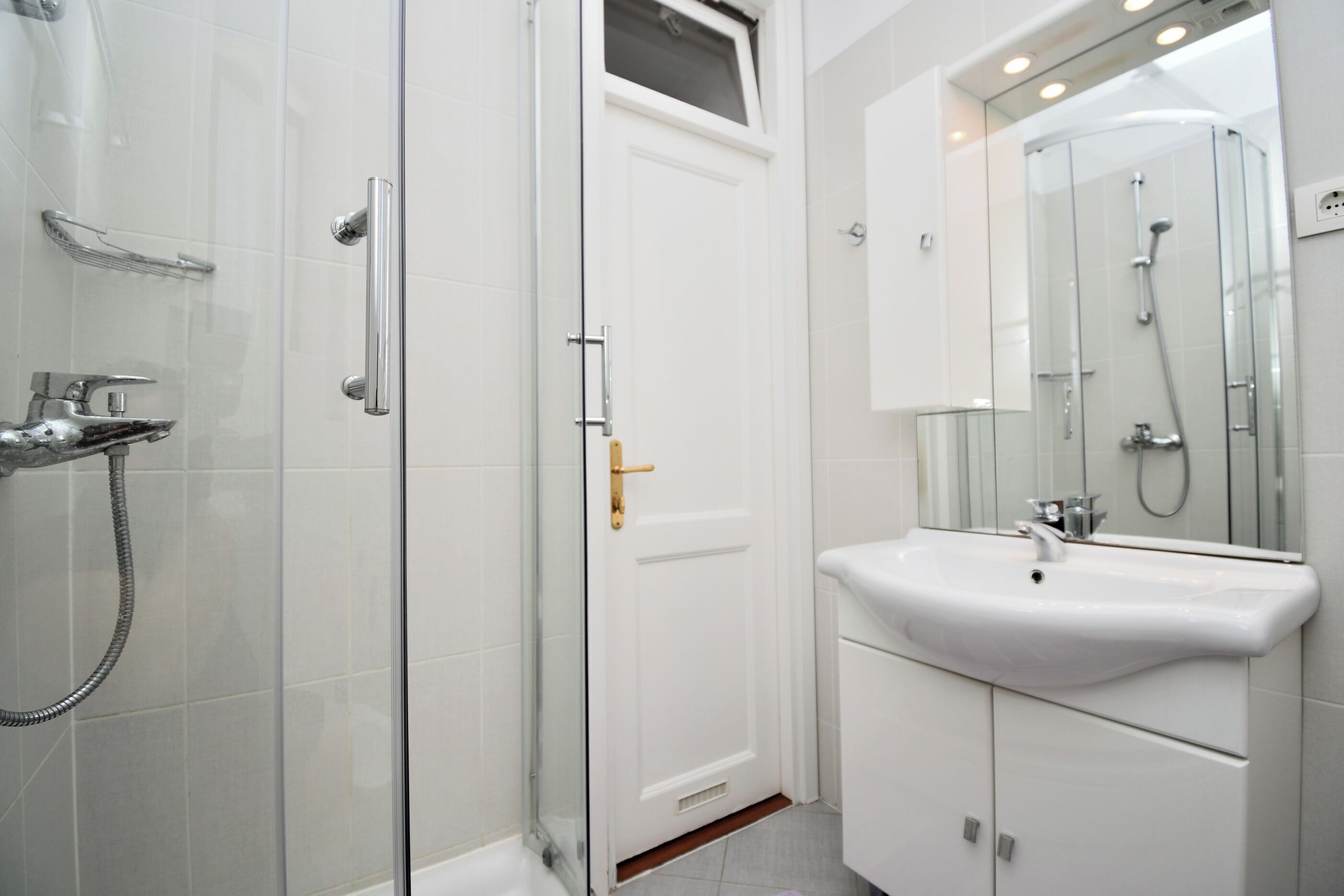 A modern bathroom with a glass shower enclosure, a white sink, and a mirror above it.