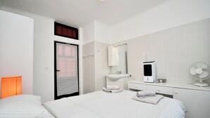 Una habitación de hotel con cama, mesita de noche, espejo, lavabo y ventilador.