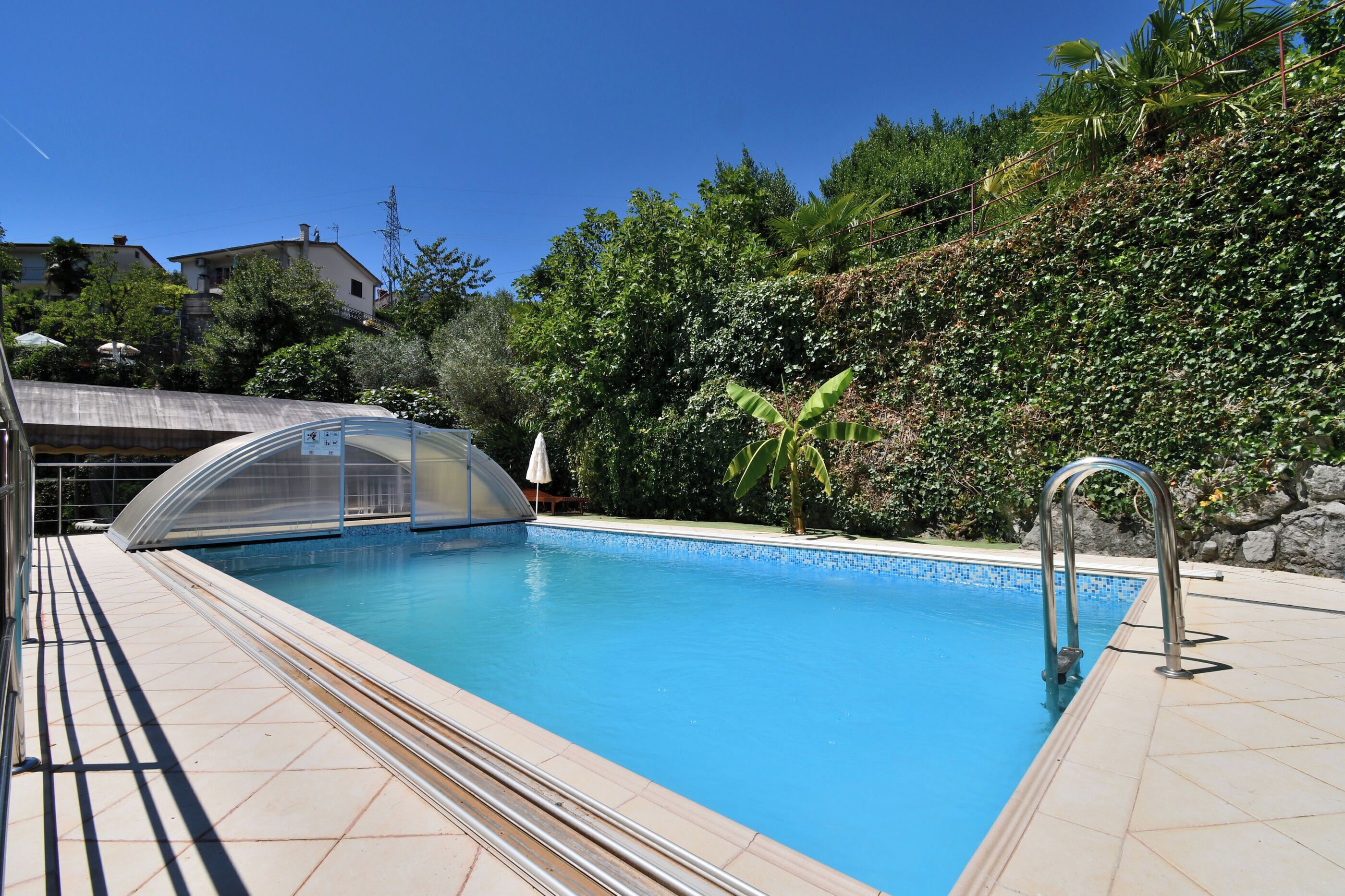 A swimming pool with a clear water surface, surrounded by a tiled deck and a metal ladder.