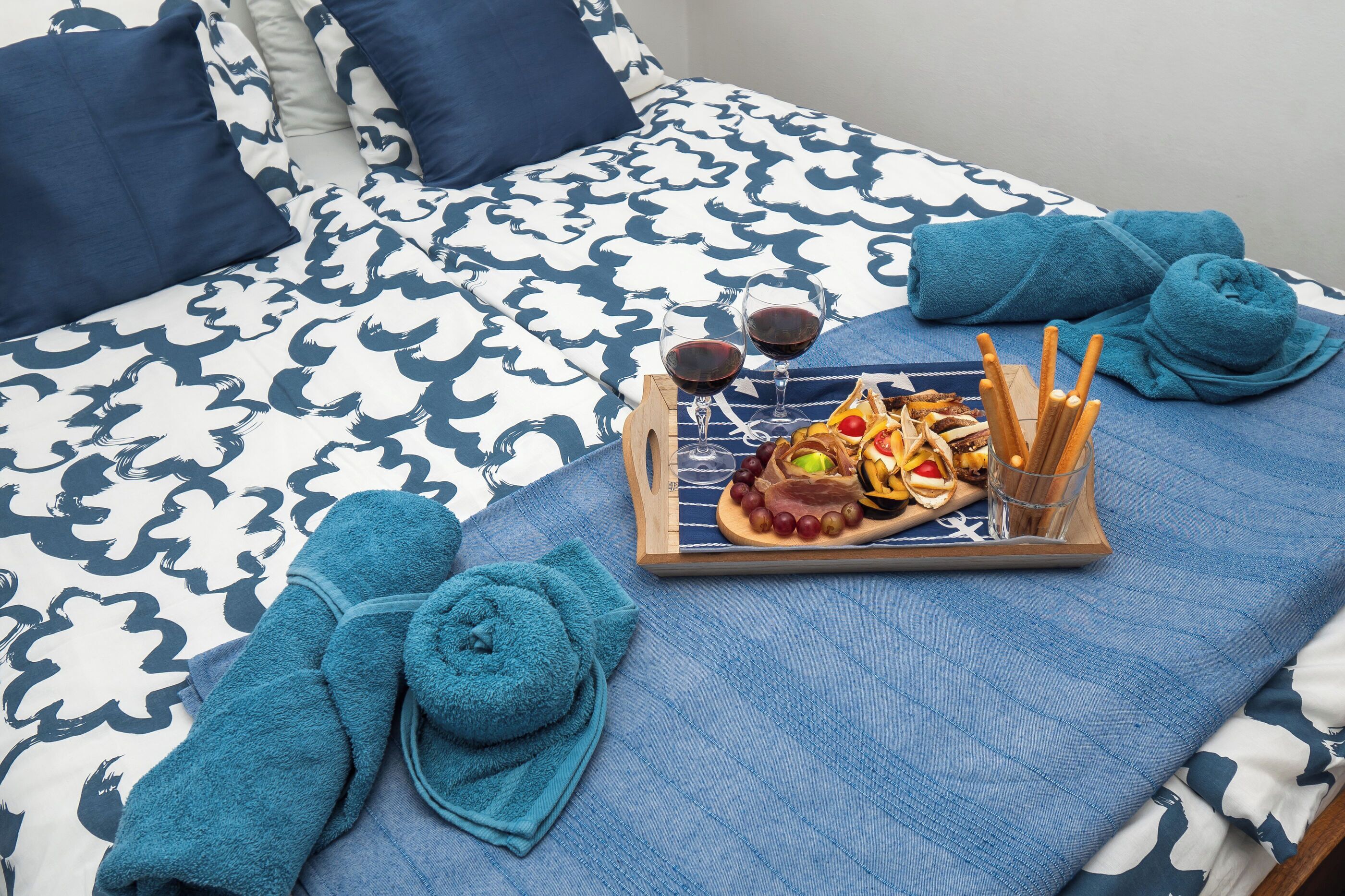 A neatly made bed with a patterned bedspread, a tray with snacks and drinks, and two rolled towels.