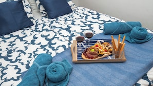 Una cama bien hecha con una colcha estampada, una bandeja con aperitivos y bebidas, y dos toallas enrolladas.