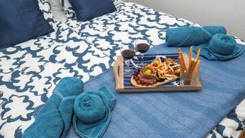 A neatly made bed with a patterned bedspread, a tray with snacks and drinks, and two rolled towels.