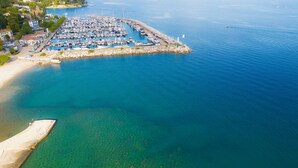 An aerial view of a marina with boats docked, a pier, and a beach area. - Apartment Darko (Opatija)