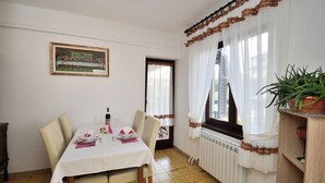 A dining room with a table set for four, a framed picture on the wall, and a potted plant on a shelf. - Apartment Elizabeta (Umag)