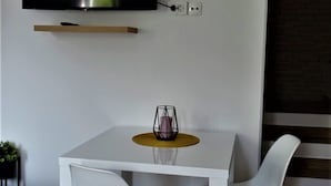 Ein modernes Zimmer mit einem weißen Tisch, zwei weißen Stühlen, einem an der Wand befestigten Fernseher und einem kleinen Schrank darunter.