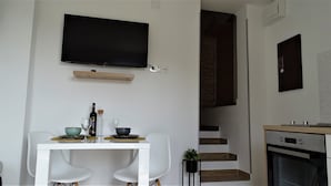 Eine moderne Küche mit Backofen, ein Essbereich mit weißen Stühlen und eine Treppe, die in ein Obergeschoss führt.