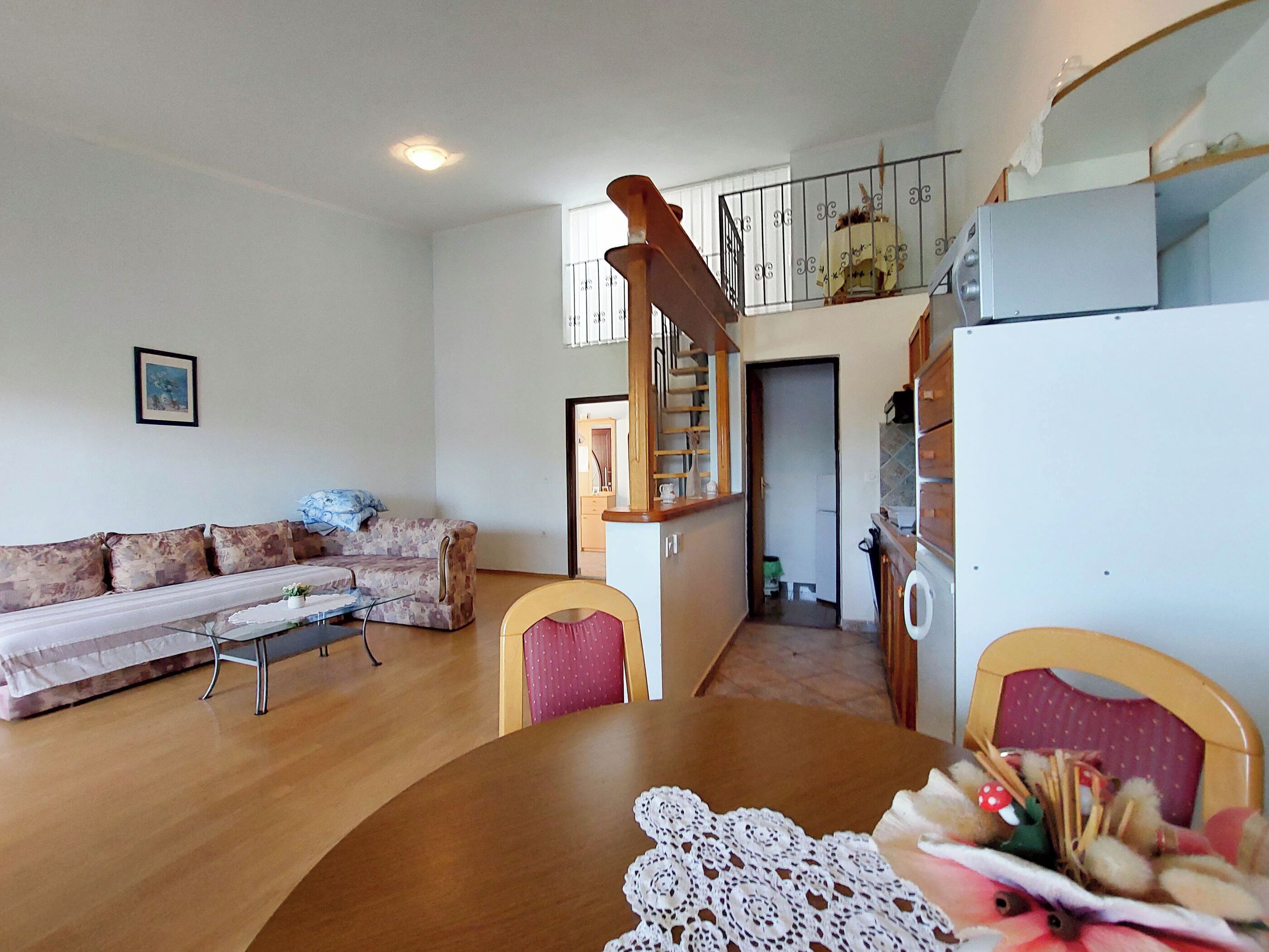 A living room with a sofa, a dining table with a lace tablecloth, a staircase, and a kitchen area.