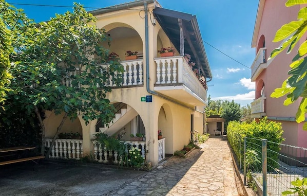 A two-story building with a balcony, a stone pathway, and a fence. - Apartments Baburic (Krk)