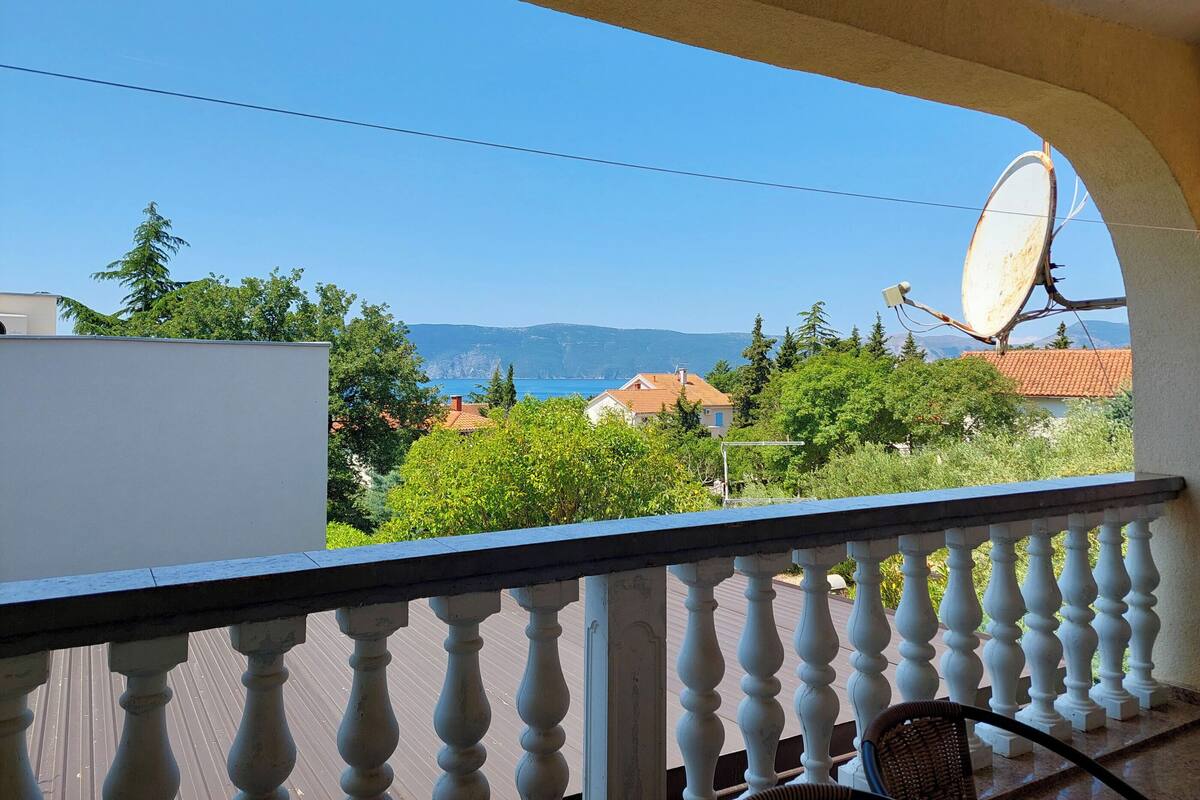 Un balcone con vista su un paesaggio costiero, che comprende case, alberi e montagne.