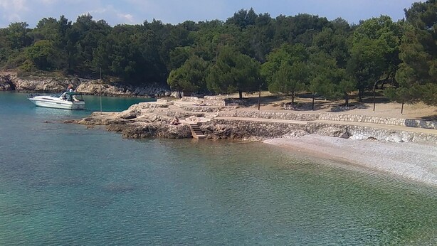 A coastal area with clear water, rocky terrain, and a boat on the water. - Apartments Baburic (Krk)