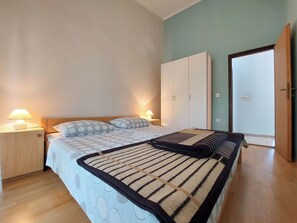 A bedroom with a bed, two bedside tables with lamps, a wardrobe, and a door. - Apartments Baburic (Krk)