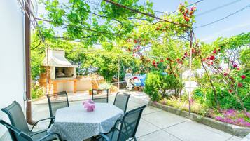 An outdoor patio with a round table and chairs, surrounded by lush greenery and flowering plants.