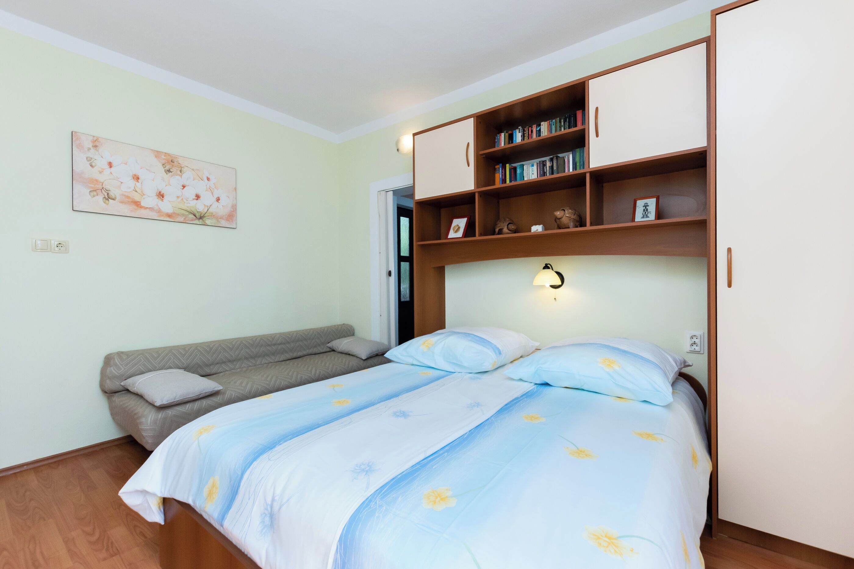 A bedroom with a bed, a sofa, a bookshelf, and a wall-mounted light.