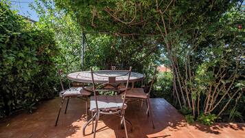 A round metal table with four chairs, surrounded by dense foliage and a tiled patio.