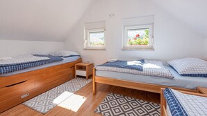 A bedroom with two beds, a wooden dresser, a bedside table, and two windows with flower boxes. - House Jasenak (Gracac)